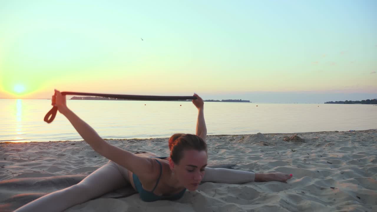 estiramiento al aire libre. banda elástica de fitness. mujer joven atlética está haciendo ejercicios usando banda elástica de fitness, en la playa durante la puesta o el amanecer. entrenamiento de fitness al aire abierto. hacer deportes por la mañana. fitness, deporte, yoga y estilo de vida saludable