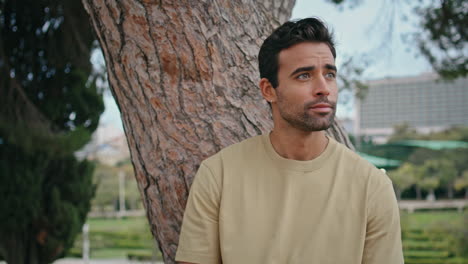 unshaven man relaxing park leaning on tree trunk close up. portrait hispanic guy