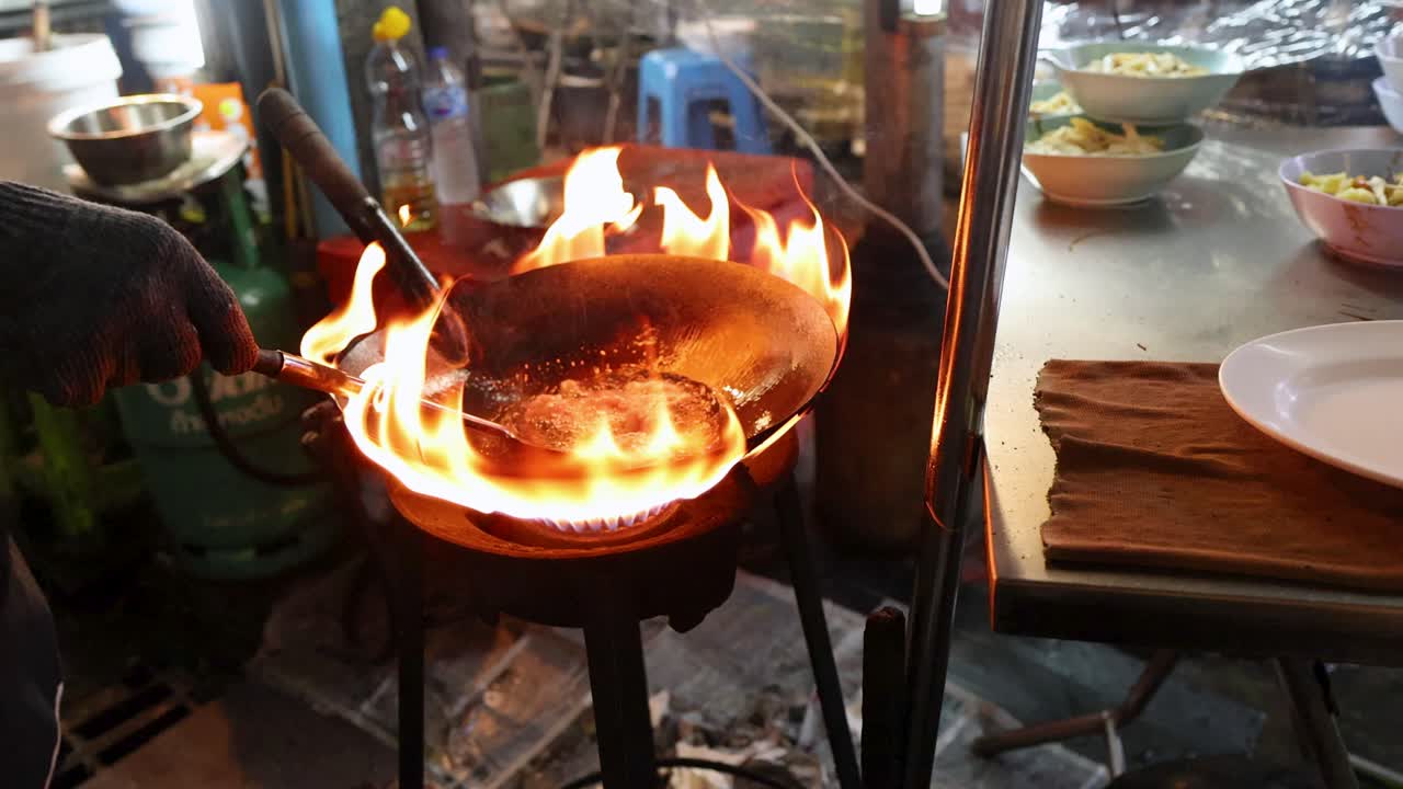Chef stir-fries ingredients in flaming wok at bustling Bangkok street food stall, dynamic lighting
