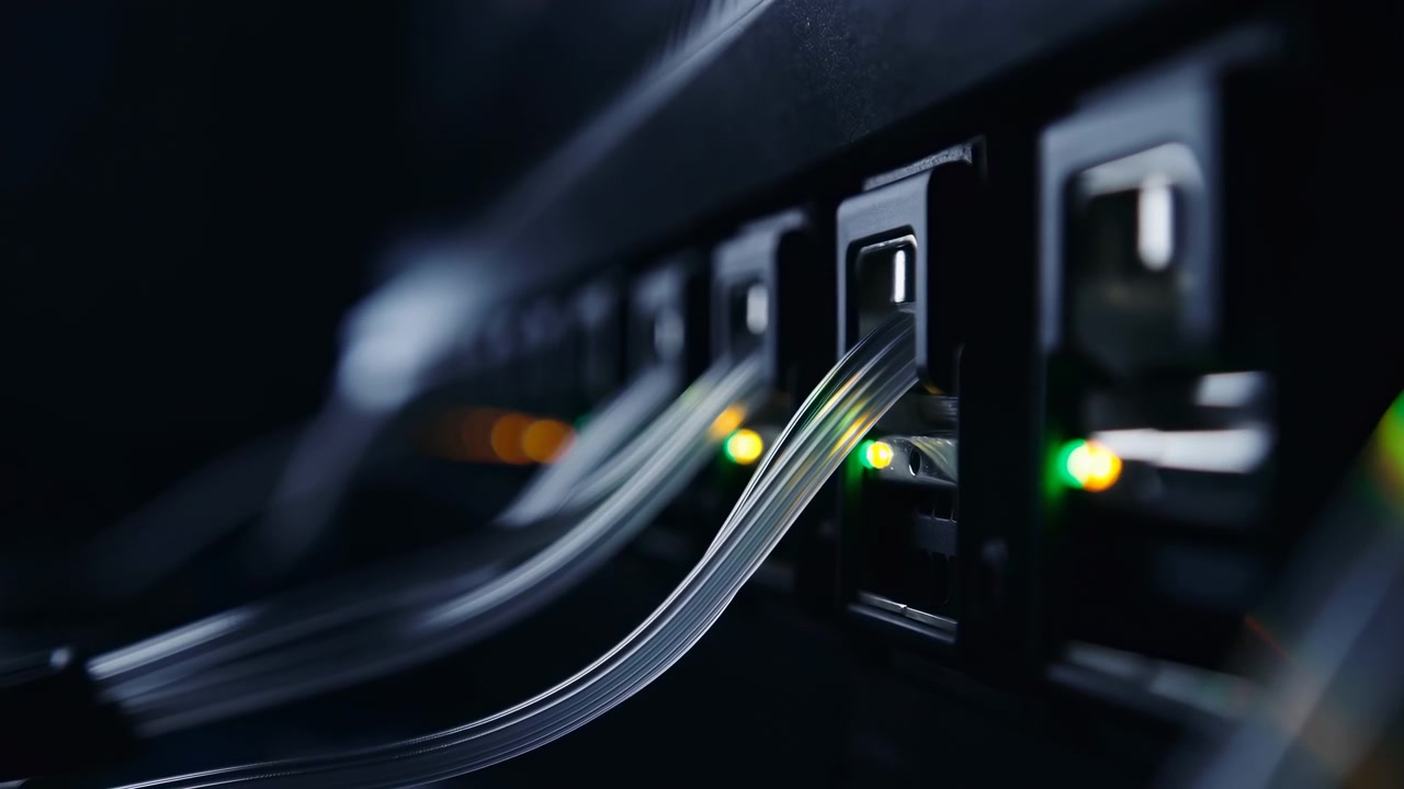 Vista ravvicinata di linee in fibra ottica curve che si muovono attraverso apparecchiature elettroniche con piccole luci colorate, sfondo scuro, superfici riflettenti e una composizione focalizzata che evidenzia la connettività digitale.