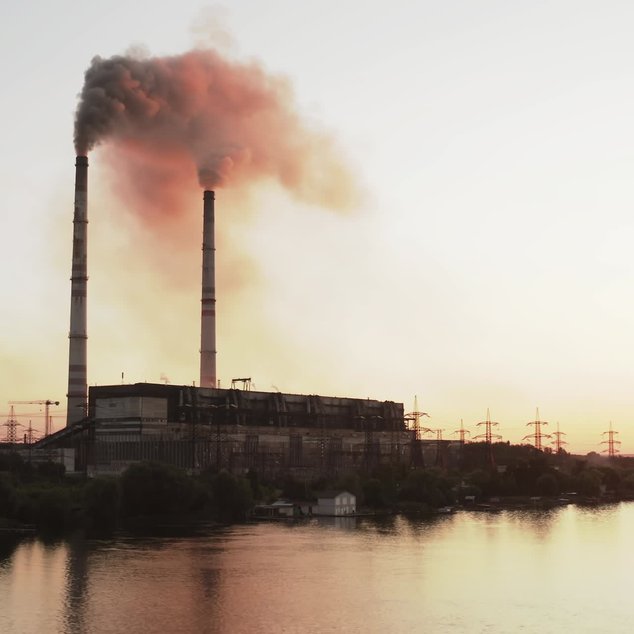 Dark puffs of smoke releases into the atmosphere. Harmful emissions from industrial plant pollute the air near the river at sunset. Ecological disaster