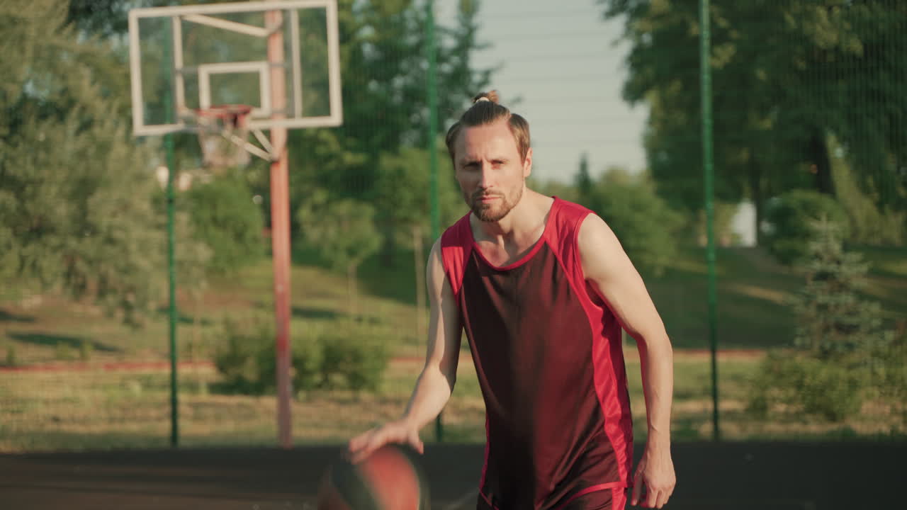 un apuesto jugador de baloncesto concentrado regateando en una cancha de baloncesto al aire libre en un día soleado