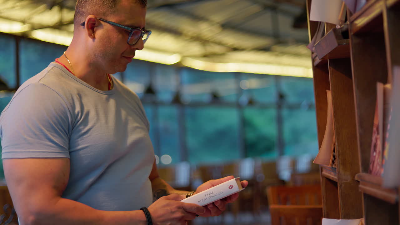 Smart adult man browsing and reading a book in a well-lit library or bookstore interior