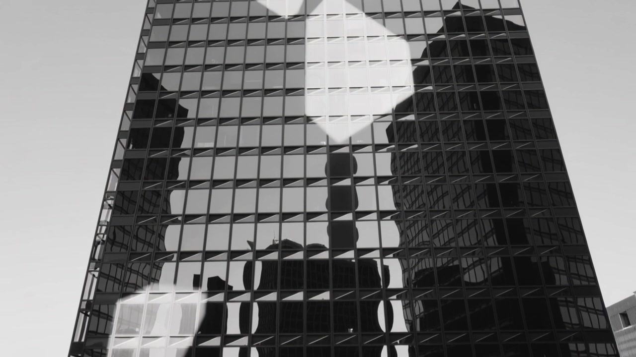 Una torre de cristal que refleja la luz del sol, proyectando dos formas brillantes hacia arriba en la calle, mostrando su columna central