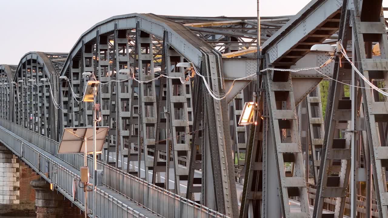 Lateral pan revealing the intricate steel framework of the iron bridge between Piacenza and Cremona, glowing in soft golden hour light
