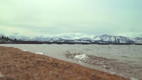 pan shot of a sandy south lake tahoe beach surrounded by the sierra nevada mountains covered in snow landscape and dramatic clouds and light