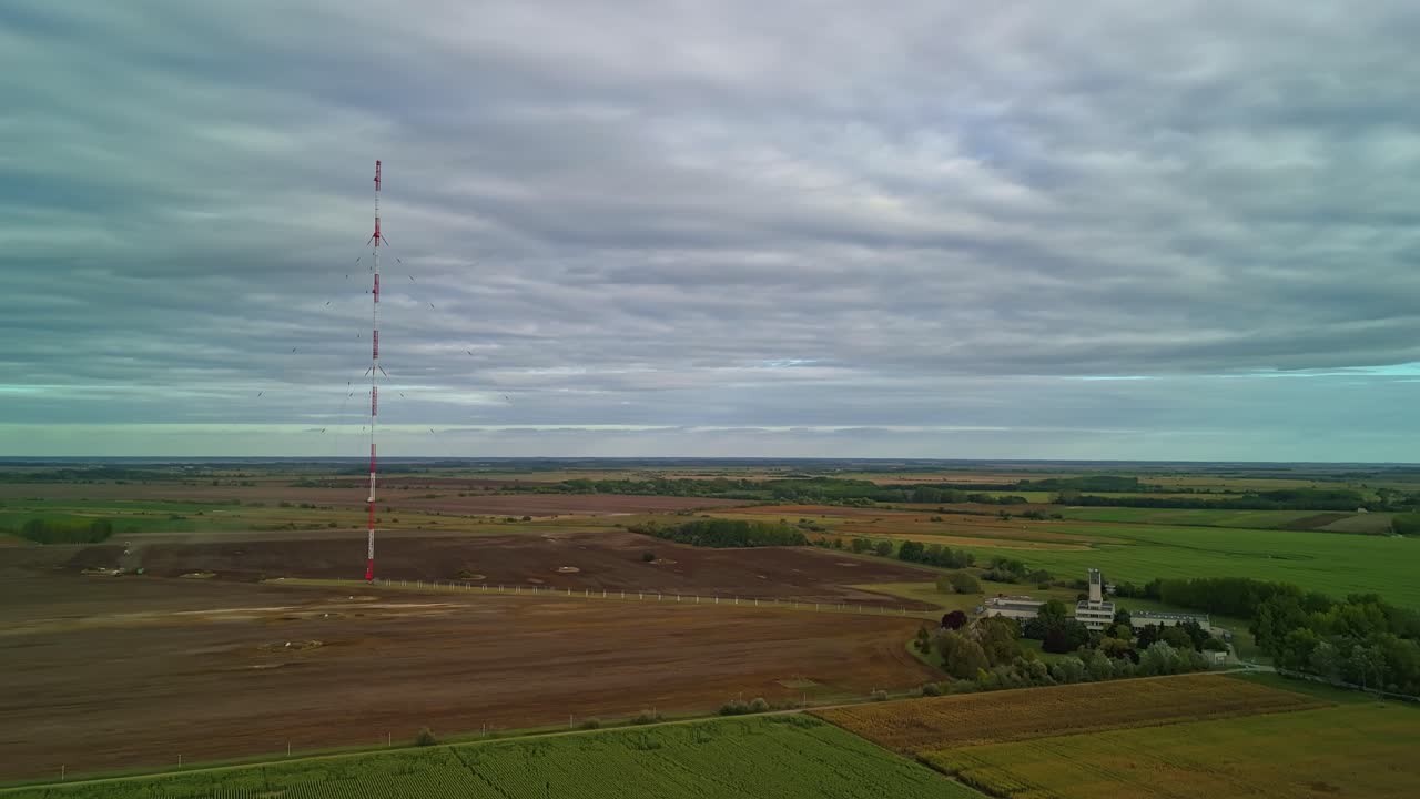 Drone hyperlapse from the Solt radio tower and the service facility building with the surrounding agricultural lands on a cloudy day in Hungary