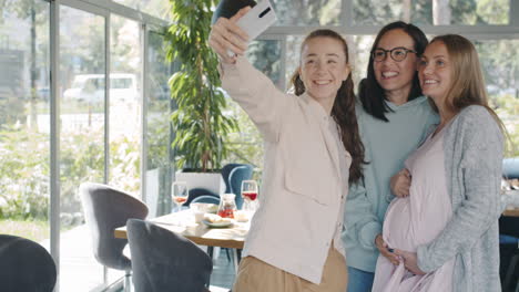 happy pregnant friends taking a selfie in a cafe
