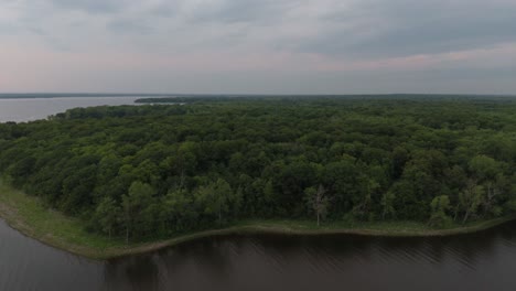 Slow-gliding-shot-of-drone-flying-sideways-showing-forest-line-on-water-shore
