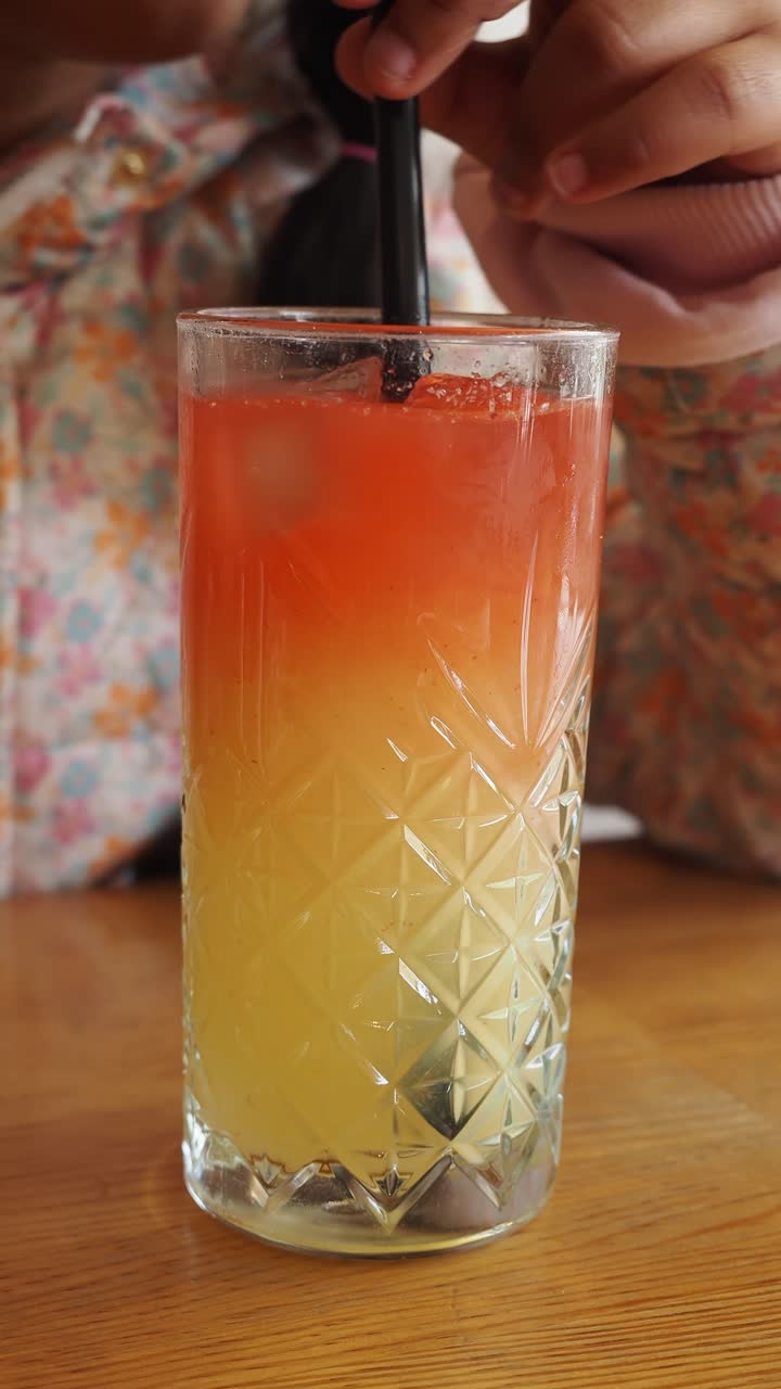 Primo piano di una persona che mescola una bevanda colorata a strati con una cannuccia