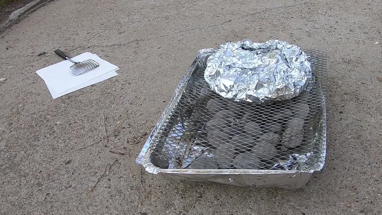 Potatos in aluminum tin foil on a throw away BBQ sitting in a driveway on a sunny day.