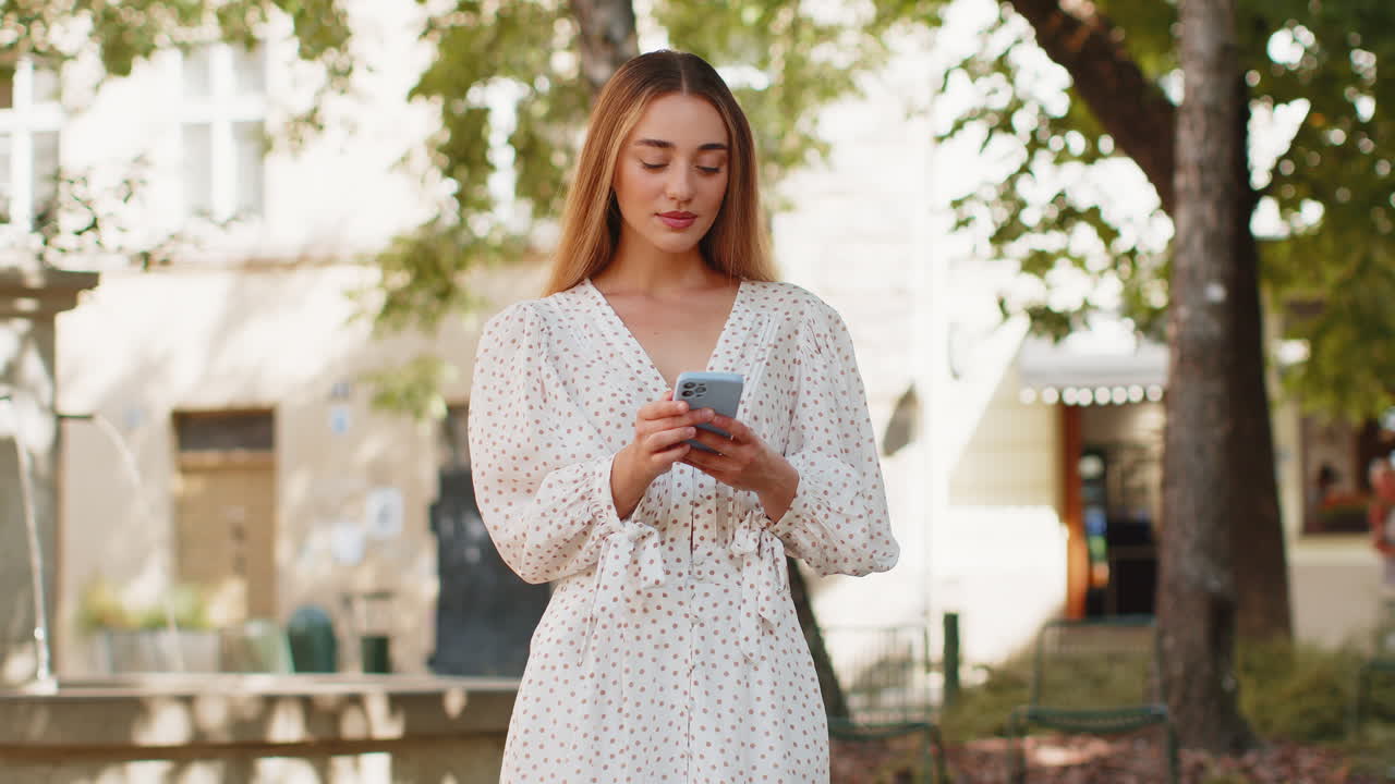 Giovane donna caucasica che usa lo smartphone, scrive messaggi sui social media, invia e-mail in una strada della città.