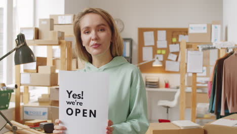 woman in office holding sign saying 'yes! we're open'