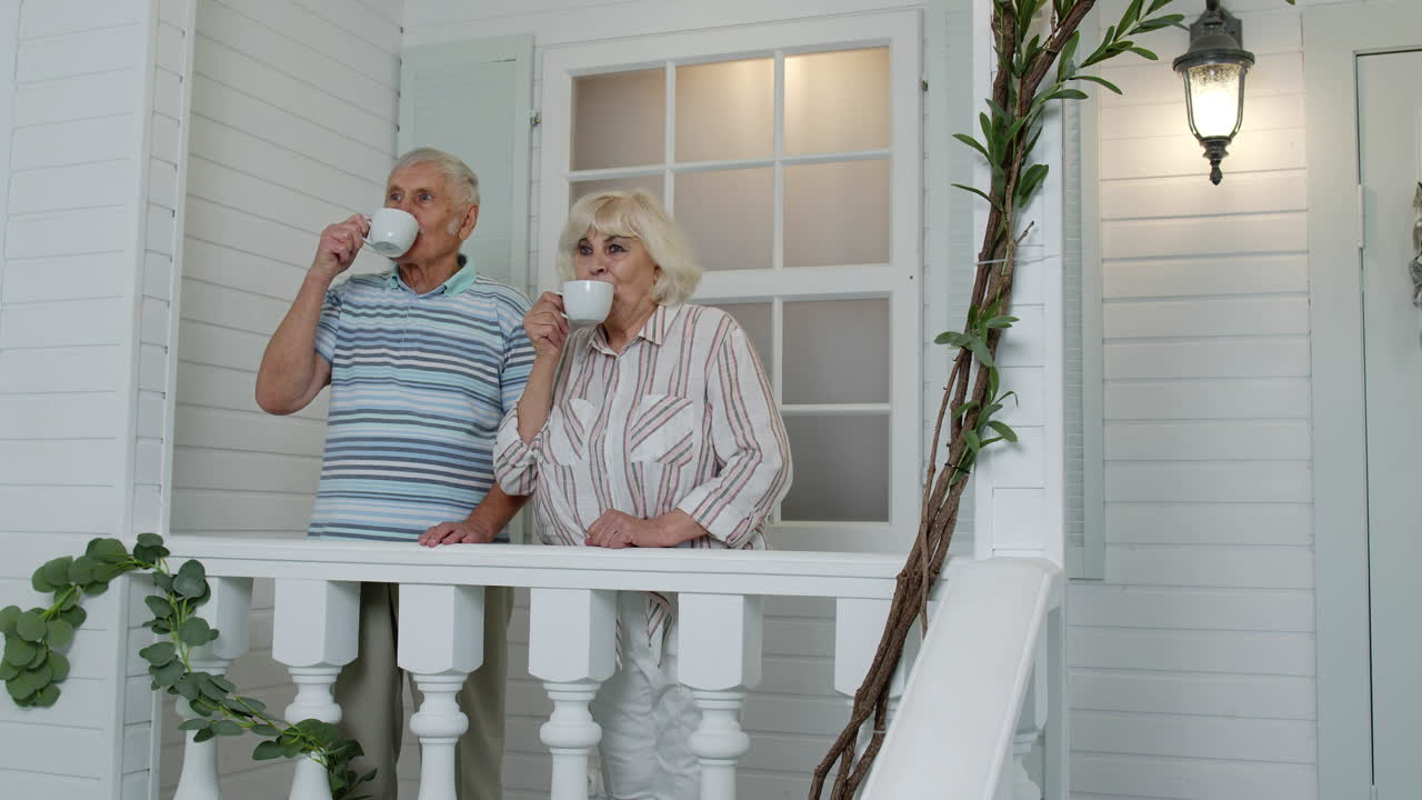 Senior elderly Caucasian couple drinking coffee, embracing in porch at home. Mature happy family