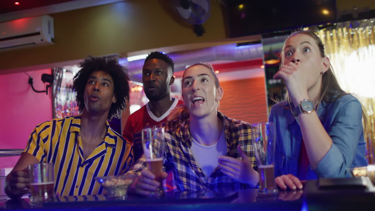 Video di un gruppo eterogeneo di amici che reagisce a una partita sportiva sullo schermo in un bar