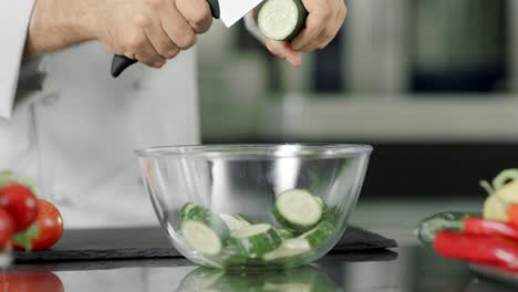 chef cortando pepino fresco en un cuenco de vidrio en cámara lenta en la cocina