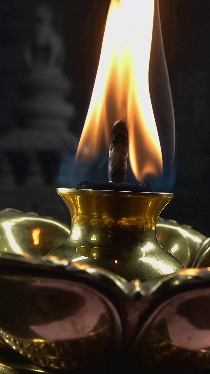 Vertical video: Smoldering wick igniting brass oil lamp at altar, blue base and yellow flame rising