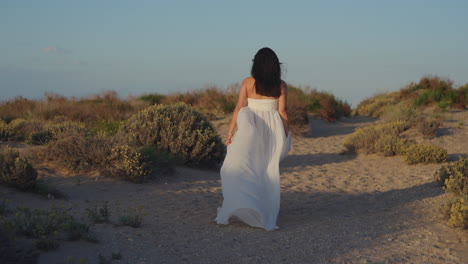 a barefoot woman in a white dress walks through the dunes at sunset - spain
