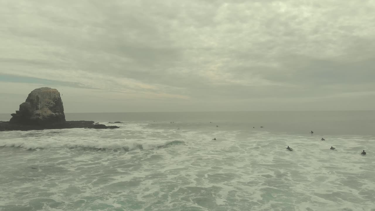 Surfers in the Ocean near a Rocky Outcrop on an Overcast Day