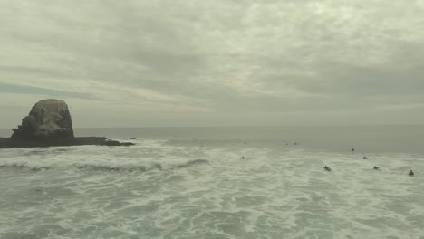 surfers in the ocean near a rocky outcrop on an overcast day