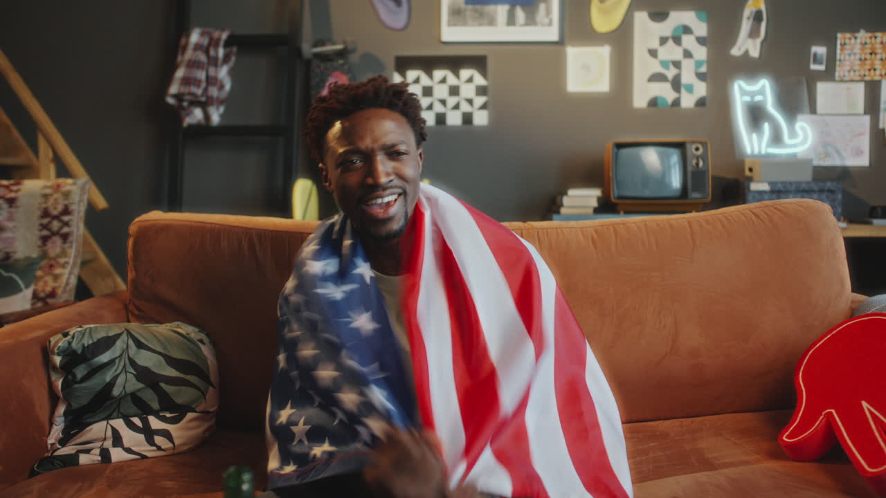 Excited Black Man Watching Sports Game on TV and Cheering with American Flag