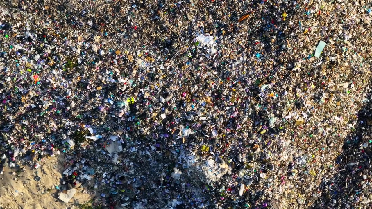 A landfill site displays significant plastic contamination. Garbage accumulation is visible. Unsanitary conditions pose risks to public health.
