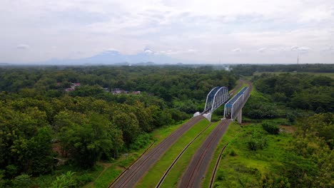 Drone-view-of-train-rail-and-bridge-over-river-in-rural-Magelang,-Central-Java