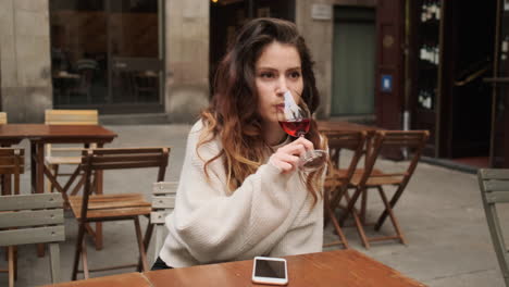 giovane ragazza che sorride alla telecamera e beve un bicchiere di vino rosso