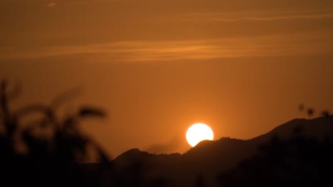 sun slowly going down behind silhouette mountain ridge, beautiful orange sunset