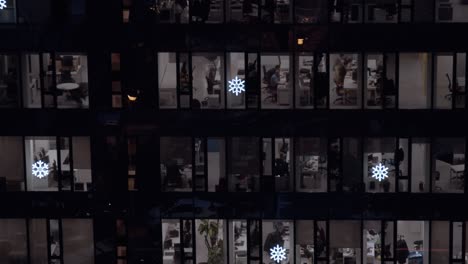 oficinas de edificios corporativos abarrotadas por muchas personas activas y trabajadoras disparadas a través de ventanas en la noche