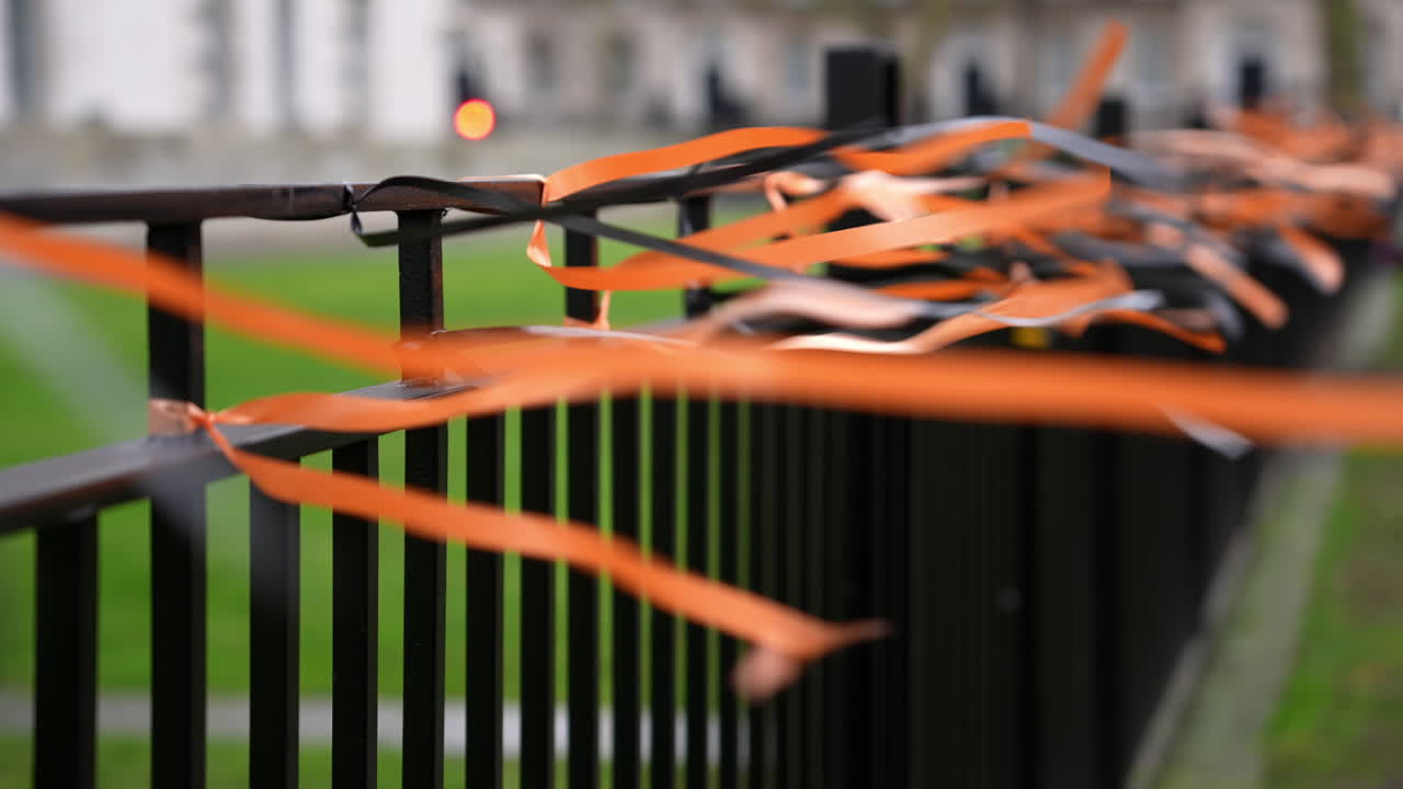 In slow motion black and orange ribbons tied to a metal fence flutter in the wind.