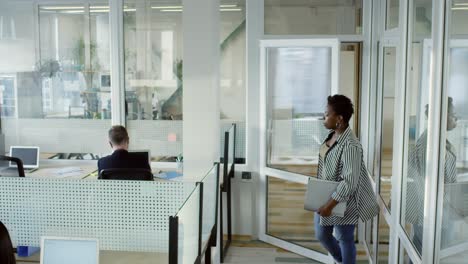 mujer de negocios africana caminando a través de la oficina de espacio abierto moderno