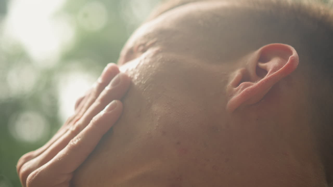 숨을 쉬기 위해 멈춰선 채 땀을 흘리는 백인 남성, 부드러운 보케와 젖은 피부를 가진 야외 러너의 인물 사진, 숨을 고르는 운동선수를 보여주는 프레임, 입을 닦는 학생, 대사를 연습하는 공연자, 햇빛이 비치는 나뭇잎, 클로즈업