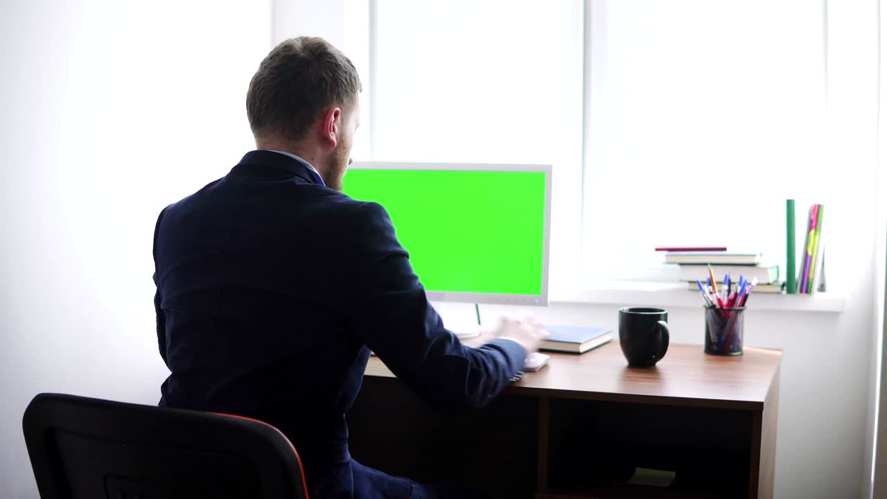 젊은이가 창 에 있는 테이블에서 녹색 화면 모형으로 컴퓨터에서 일하고 있다. 백인 노동자가 키보드에 타이핑하고 녹색 스크린을 보고 있다.