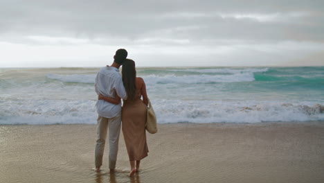 Tierna-Familia-Mirando-La-Playa-Del-Mar-Al-Amanecer.-Vista-Posterior-Pareja-Abrazándose-Por-La-Mañana