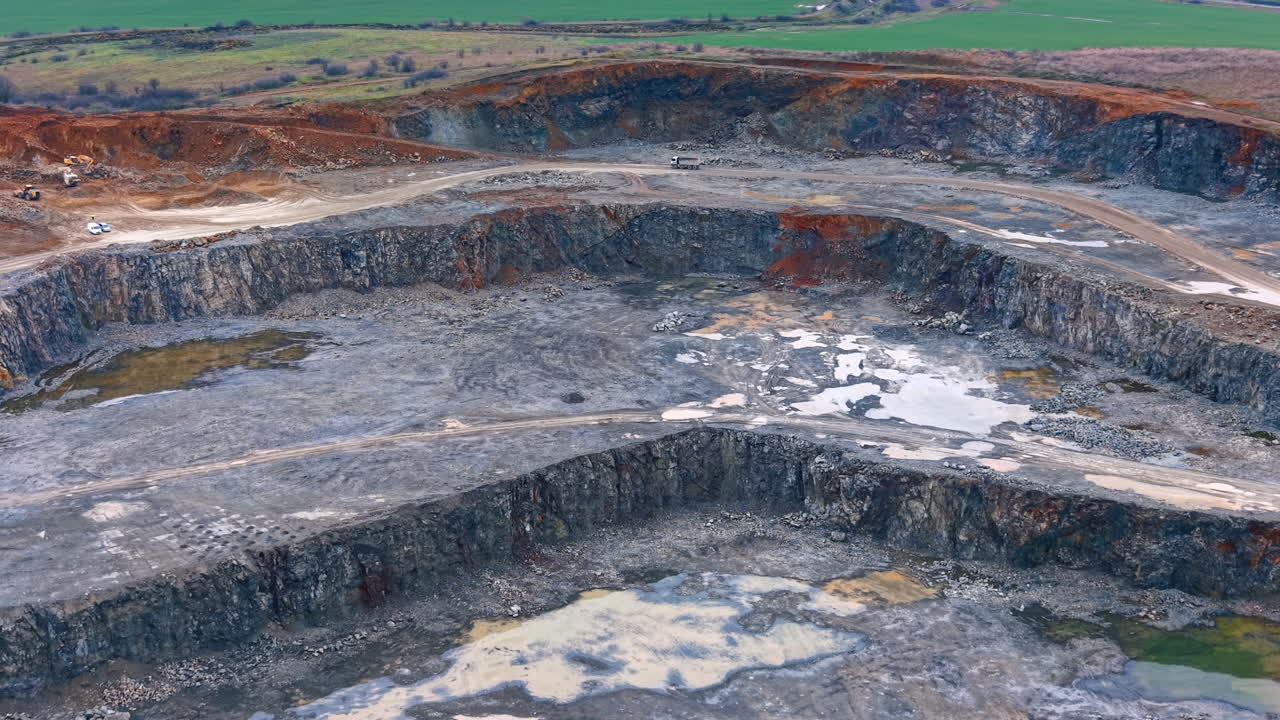 Rural open pit mining site. Workers are seen in a large pit mine extracting materials. The landscape shows layers of rocks and empty spaces