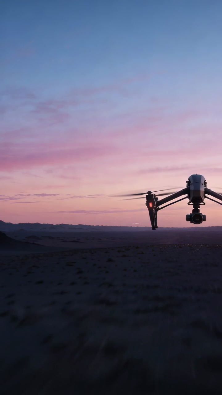 Vertical video: Hovering drone with spinning rotors and gimbal, filming desert at dusk, copy space