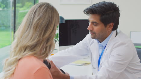 male doctor or gp examining mature female patient taking blood pressure with sphygmomanometer