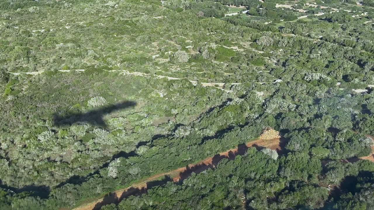 Left side view from cockpit of the shadow of a jet on the groung ablout to land, flying over green fileds