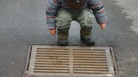 curious toddler boy looking down a storm drain