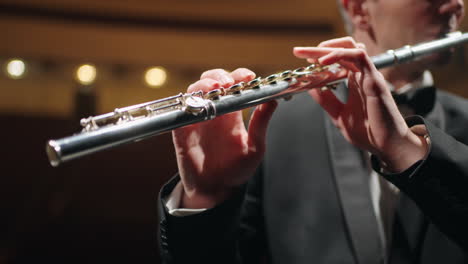 flautista está tocando en una orquesta sinfónica o banda de instrumentos de bronce vista de cerca de la flauta en manos masculinas