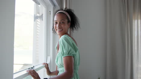 smiling woman in green dress enjoying fresh air by open window at home