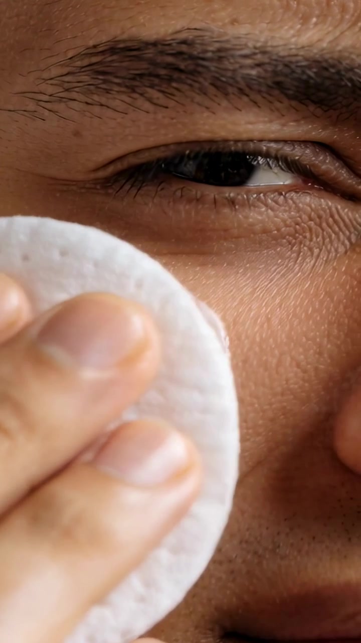 Vertical video: Placing cotton pad, adult man pressing and wiping cheek at vanity, removing cream