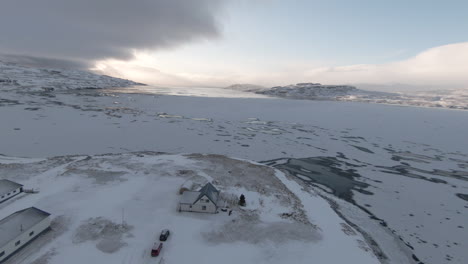 pan left, snow-covered house on frozen fjord, mountains background at sunrise