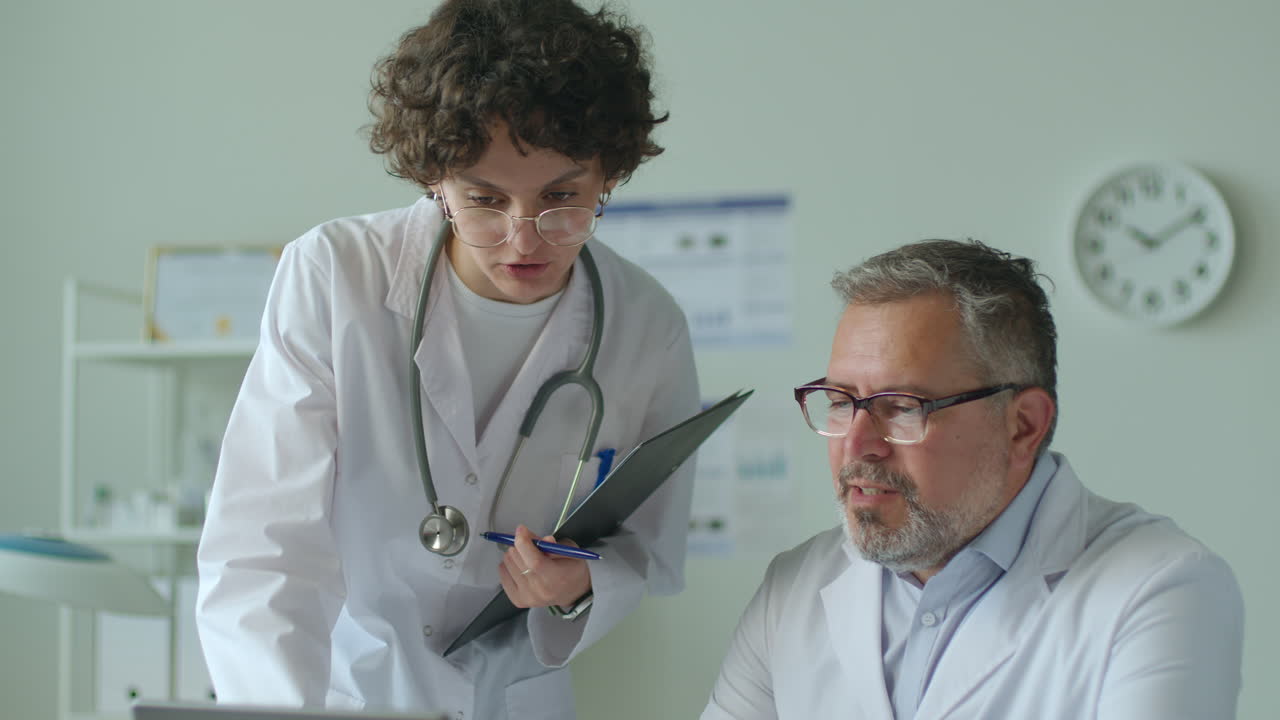 Senior Doctor Discussing Data on Laptop with Young Female Assistant