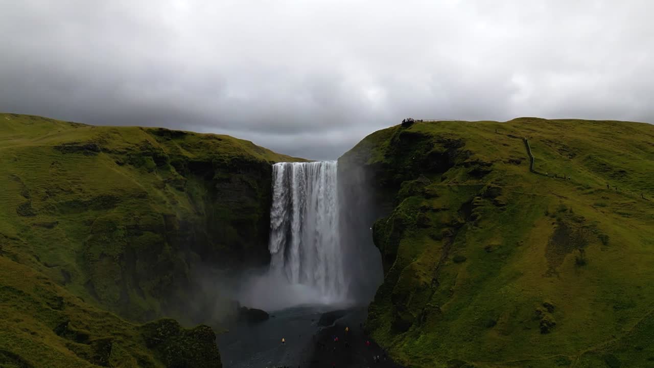4K cinematic drone footage of Skógafoss Waterfall in Iceland, capturing the immense curtain of water cascading from towering cliffs surrounded by lush green landscapes. Iceland_27