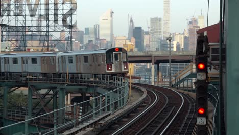 Incoming-seven-Train-at-Queensboro-Plaza-subway-station-with-the-Silvercup-Studios-and-the-Manhattan-skyline-in-the-background,-filmed-in-the-early-morning-hours-of-a-sunny-day-in-New-York-City