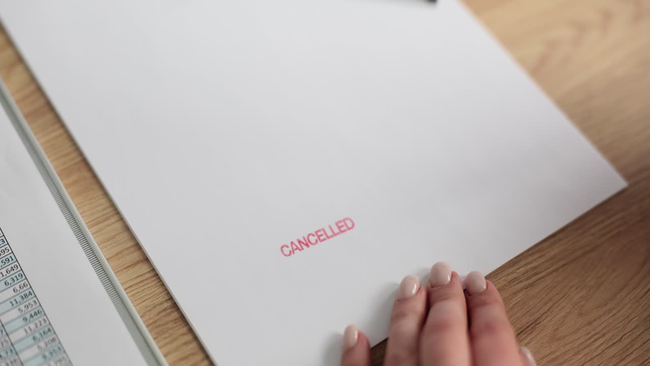 A hand stamps 'CANCELLED' on a document