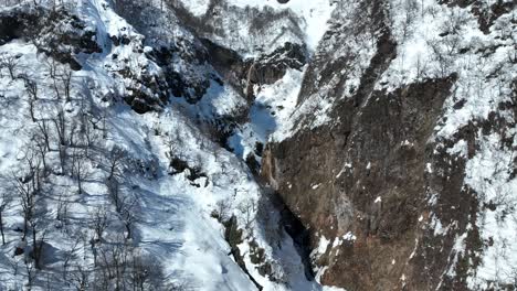 Push-in-shot-of-waterfall-from-melting-snow,-camera-flying-through-gorge-revealing-waterfall-area