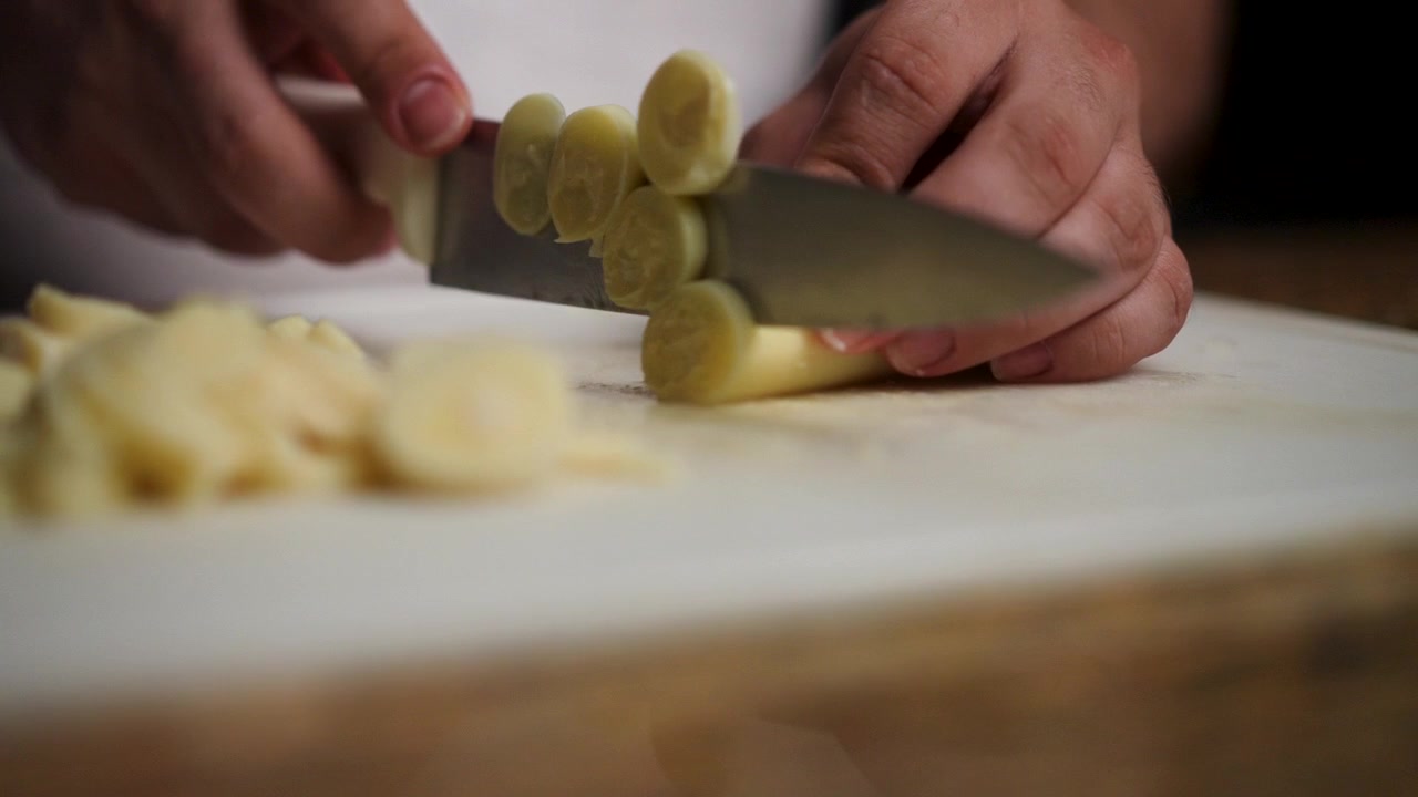 Primo piano di uno chef che affetta cuori di palma con un coltello affilato, enfatizzando il processo di preparazione di ingredienti esotici per una ricetta gourmet.